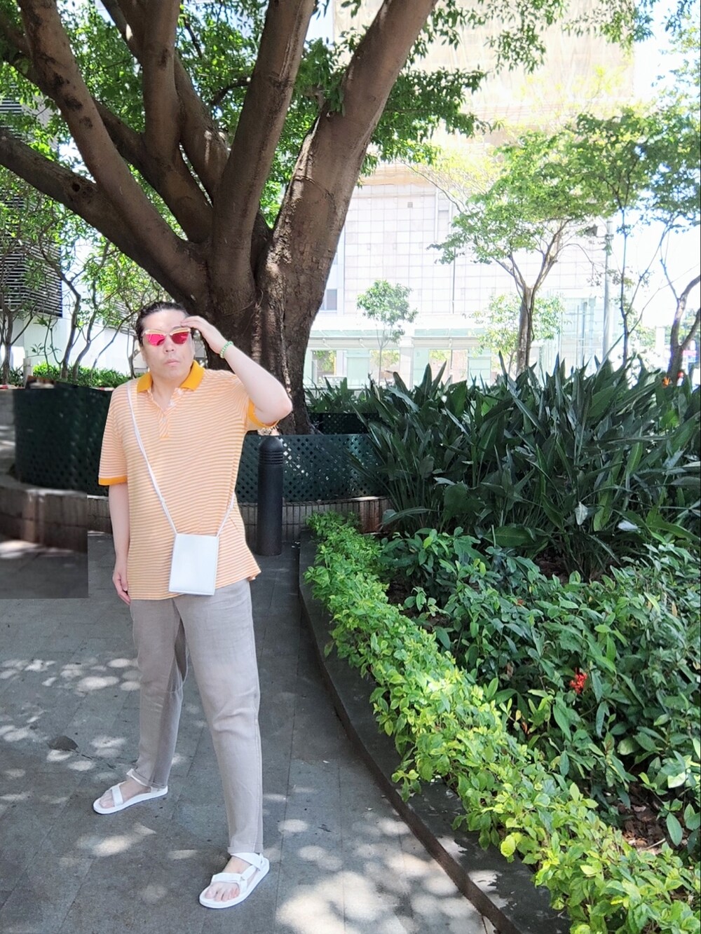 ホワイト系のバッグ、オレンジ系のポロシャツ、ベージュ系のチノパンツを着用したメンズの夏コーディネートの2枚目の写真