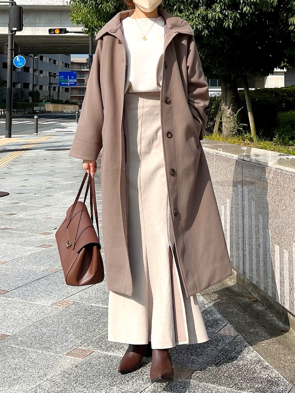 ブラウン系のステンカラーコート、ベージュ系のスカート、ブラウン系のブーツを着用したレディースの秋コーディネートの2枚目の写真