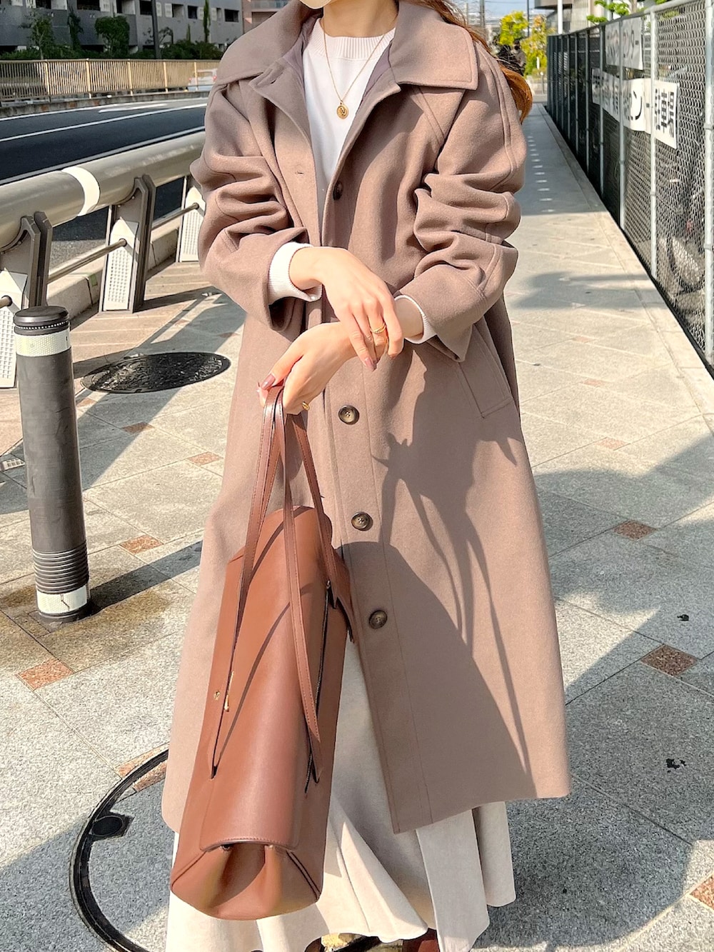 ブラウン系のステンカラーコート、ベージュ系のスカート、ブラウン系のブーツを着用したレディースの秋コーディネートの3枚目の写真