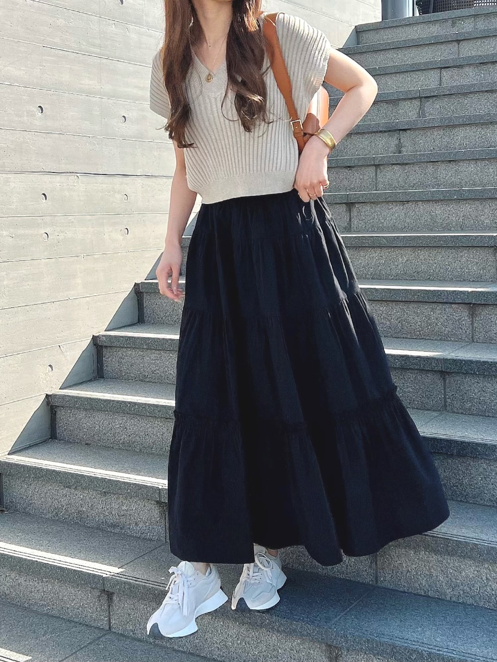 ブラック系のスカート、ベージュ系のスニーカー、ゴールド系のネックレスを着用したレディースの春コーディネートの2枚目の写真