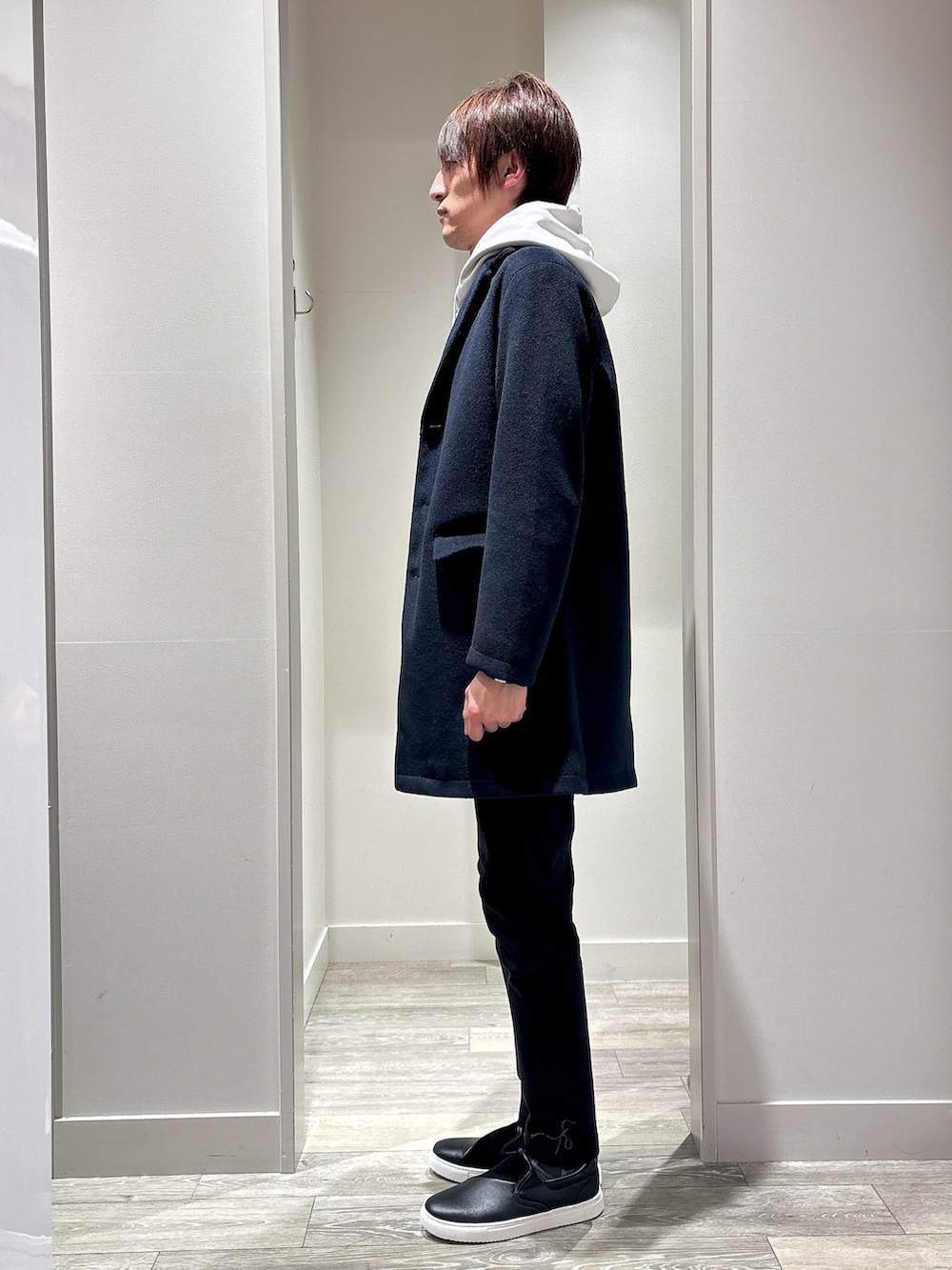 ブルー系のチェスターコート、ベージュ系のパーカー、ブラック系のチノパンツを着用したメンズの冬コーディネートの2枚目の写真