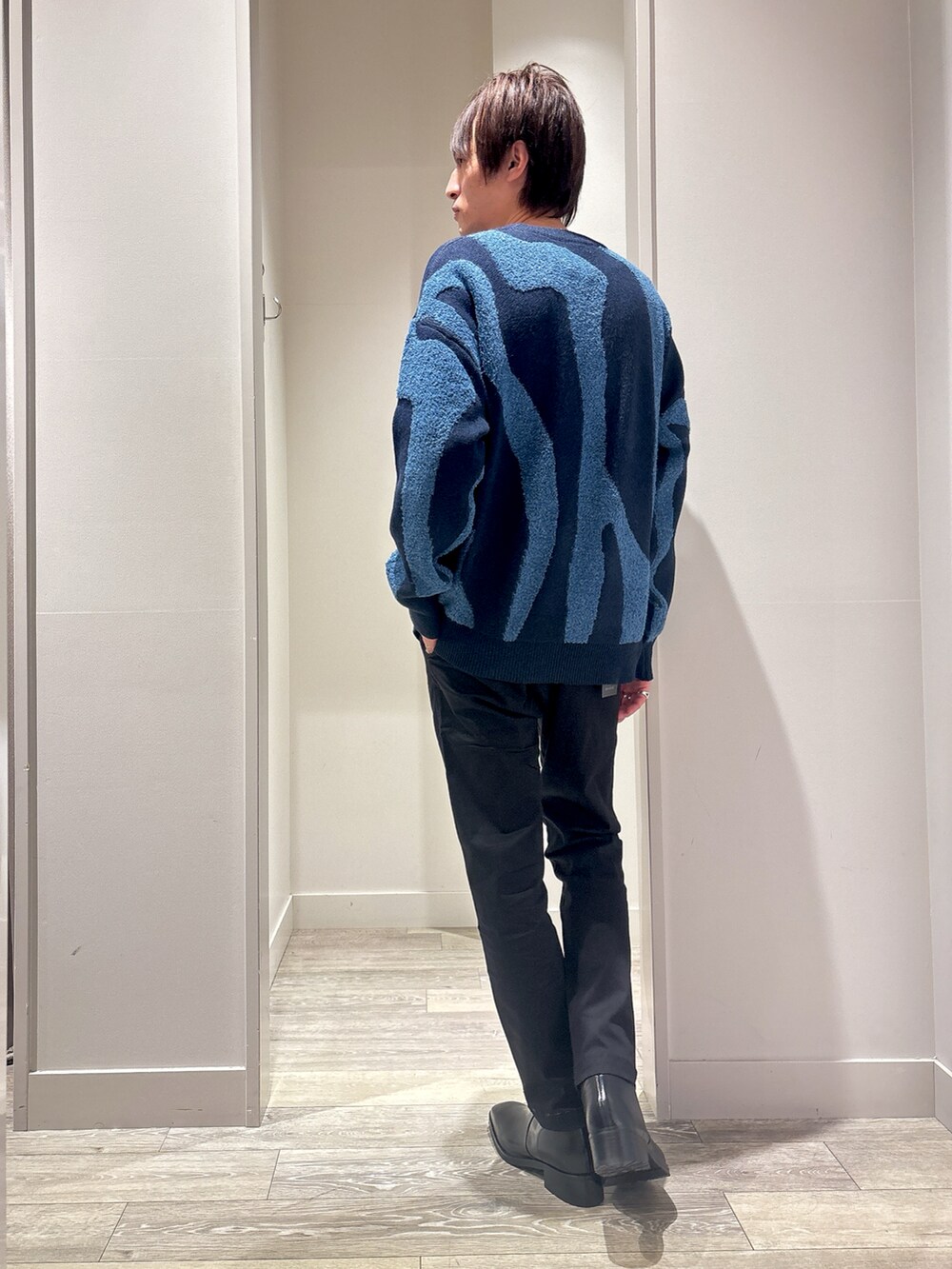 ブルー系のニット/セーター、ブラック系のチノパンツ、ブラック系のブーツを着用したメンズの冬コーディネートの2枚目の写真