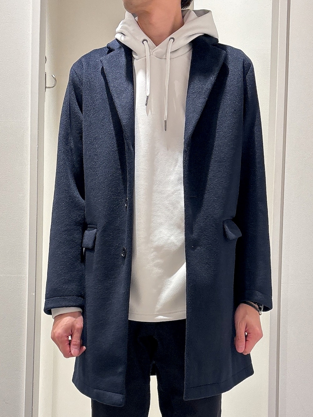 ブルー系のチェスターコート、ベージュ系のパーカー、ブラック系のチノパンツを着用したメンズの冬コーディネートの4枚目の写真