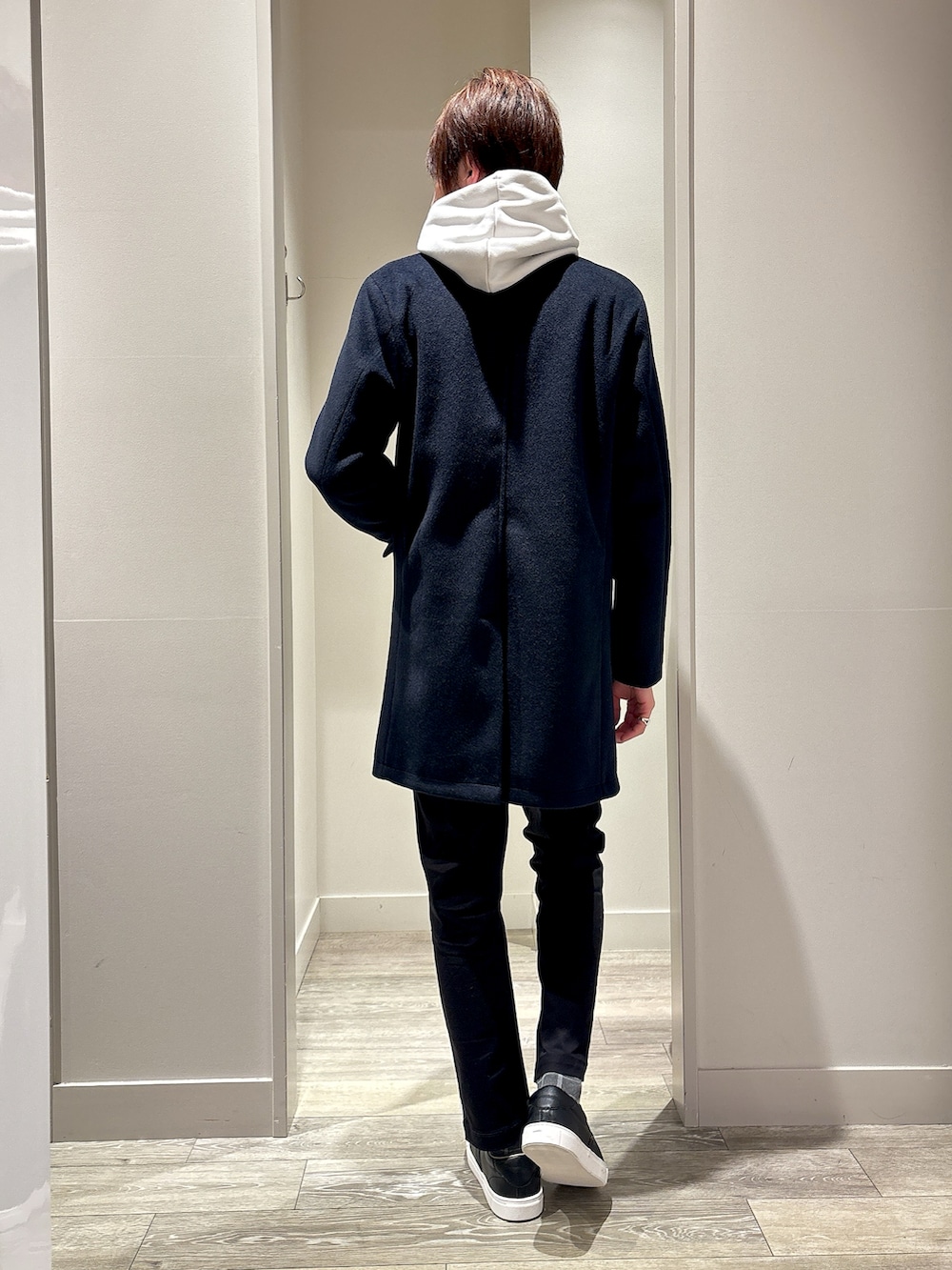 ブルー系のチェスターコート、ベージュ系のパーカー、ブラック系のチノパンツを着用したメンズの冬コーディネートの3枚目の写真