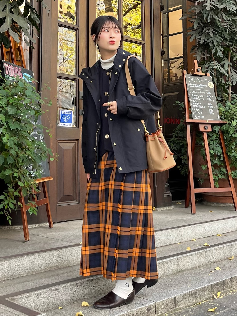 ブラック系のマウンテンパーカー、グリーン系のショルダーバッグ、オレンジ系のスカートを着用したレディースの冬コーディネートの2枚目の写真