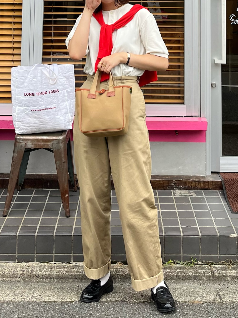 グリーン系のトートバッグ、ホワイト系のTシャツ/カットソー、ベージュ系のチノパンツを着用したレディースの夏コーディネートの2枚目の写真