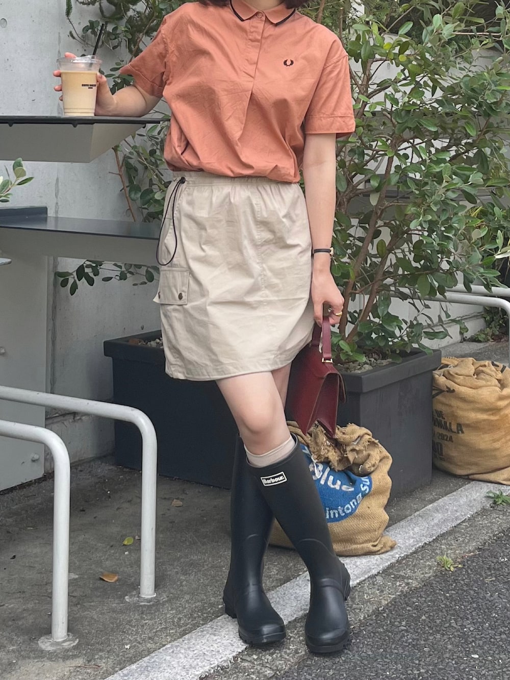 ベージュ系のスカート、オレンジ系のシャツ/ブラウス、ブラック系のブーツを着用したレディースの夏コーディネートの2枚目の写真