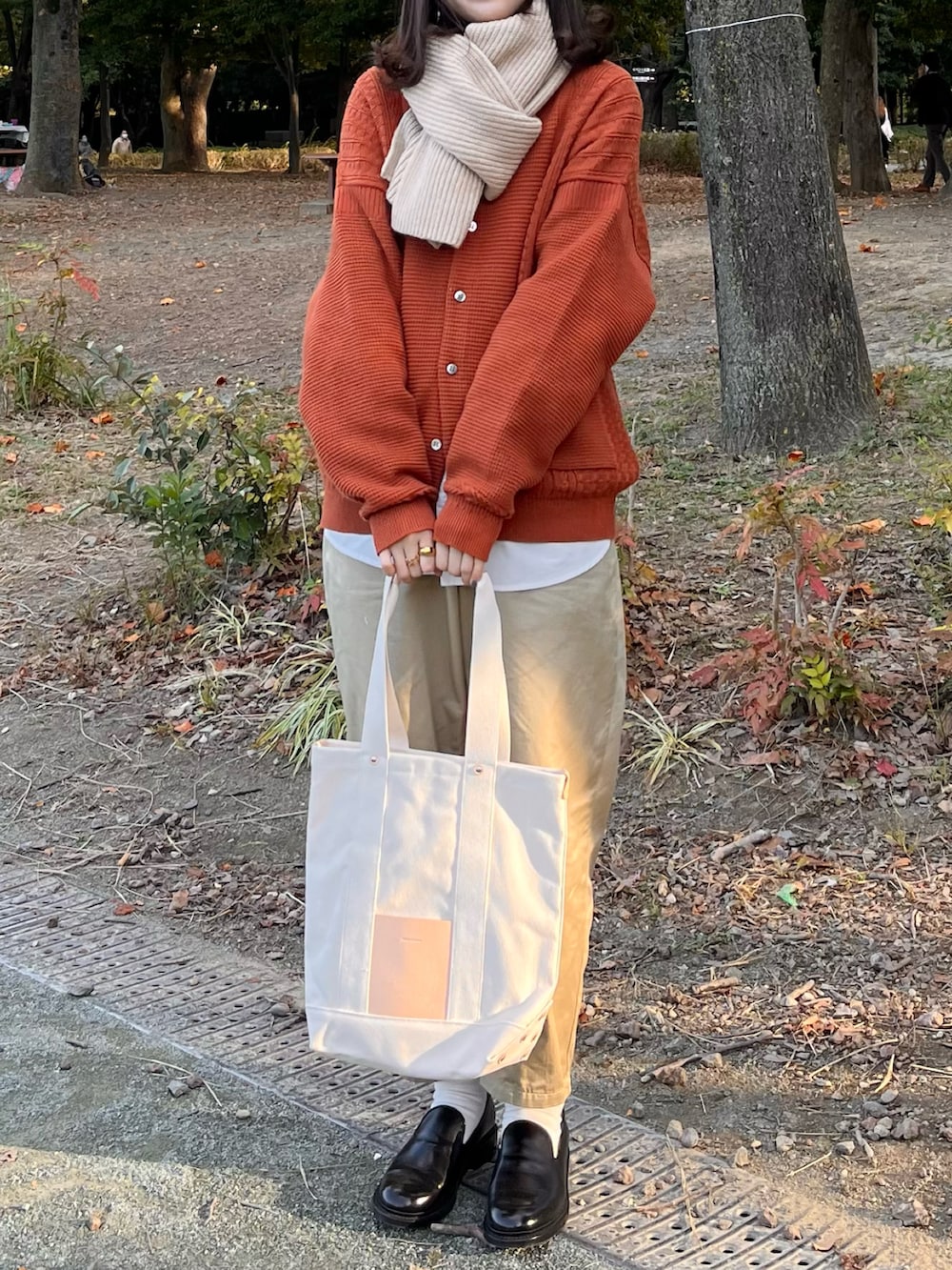 ベージュ系のチノパンツ、ホワイト系のシャツ/ブラウス、ベージュ系のトートバッグを着用したレディースの秋コーディネートの2枚目の写真