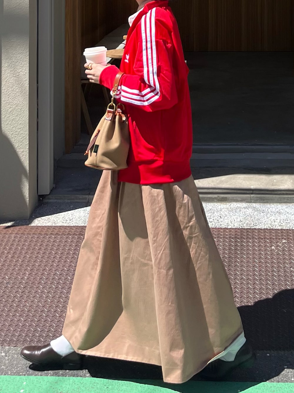 ベージュ系のスカート、レッド系のジャージ、グリーン系のショルダーバッグを着用したレディースの春コーディネートの2枚目の写真