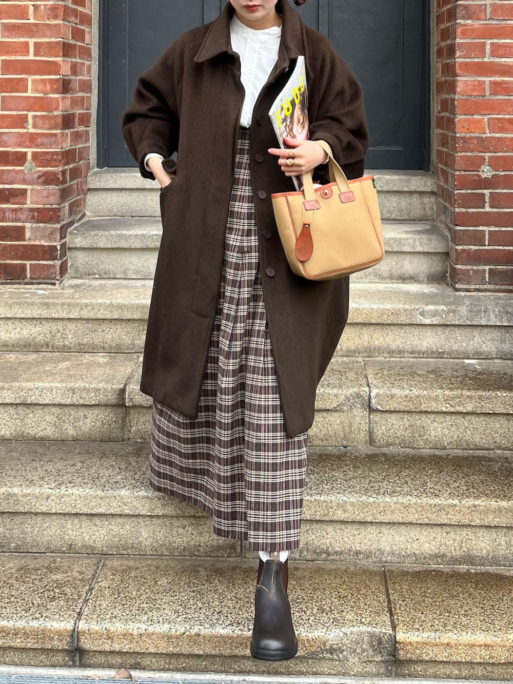 グリーン系のトートバッグ、ブラウン系のステンカラーコート、ブラウン系のブーツを着用したレディースの冬コーディネートの2枚目の写真