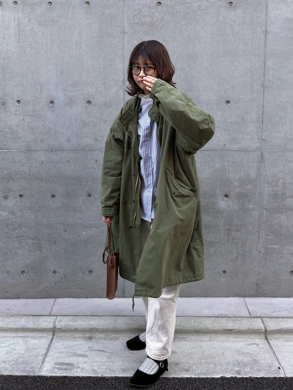 グリーン系のモッズコート、イエロー系のハンドバッグ、ブラック系のバレエシューズを着用したレディースの春コーディネートの2枚目の写真