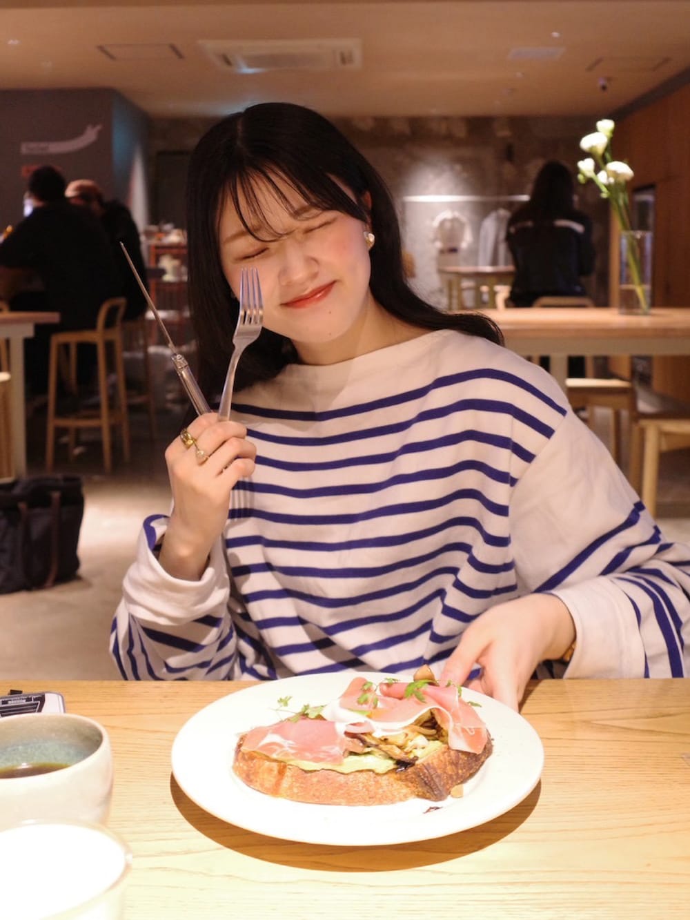 ベージュ系のチノパンツ、ブラウン系のブーツ、ブラウン系のハンドバッグを着用したレディースの春コーディネートの2枚目の写真