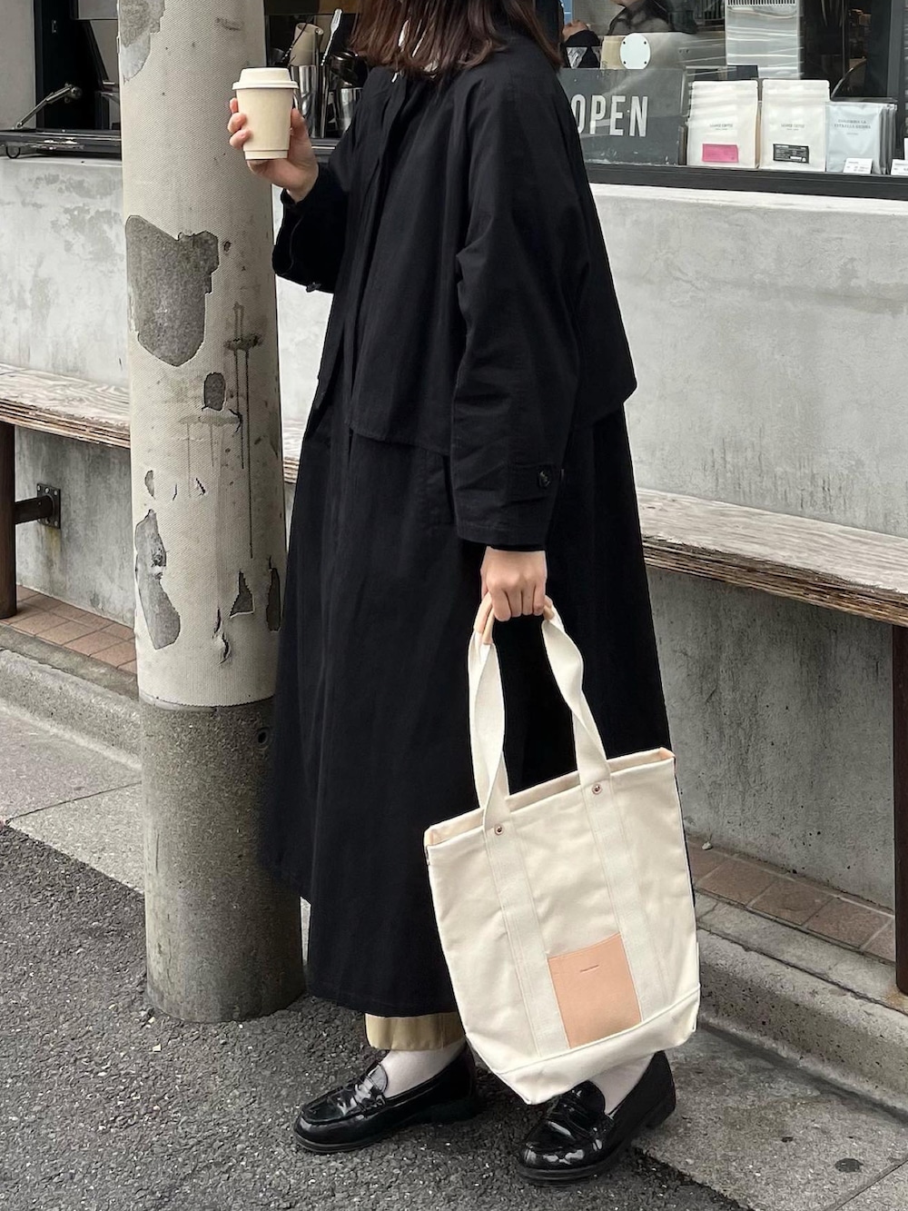 ブラック系のトレンチコート、ベージュ系のトートバッグ、ベージュ系のチノパンツを着用したレディースの秋コーディネートの2枚目の写真