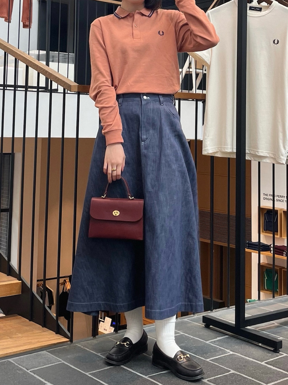 ブラック系のローファー、ブルー系のスカート、レッド系のショルダーバッグを着用したレディースの春コーディネートの2枚目の写真