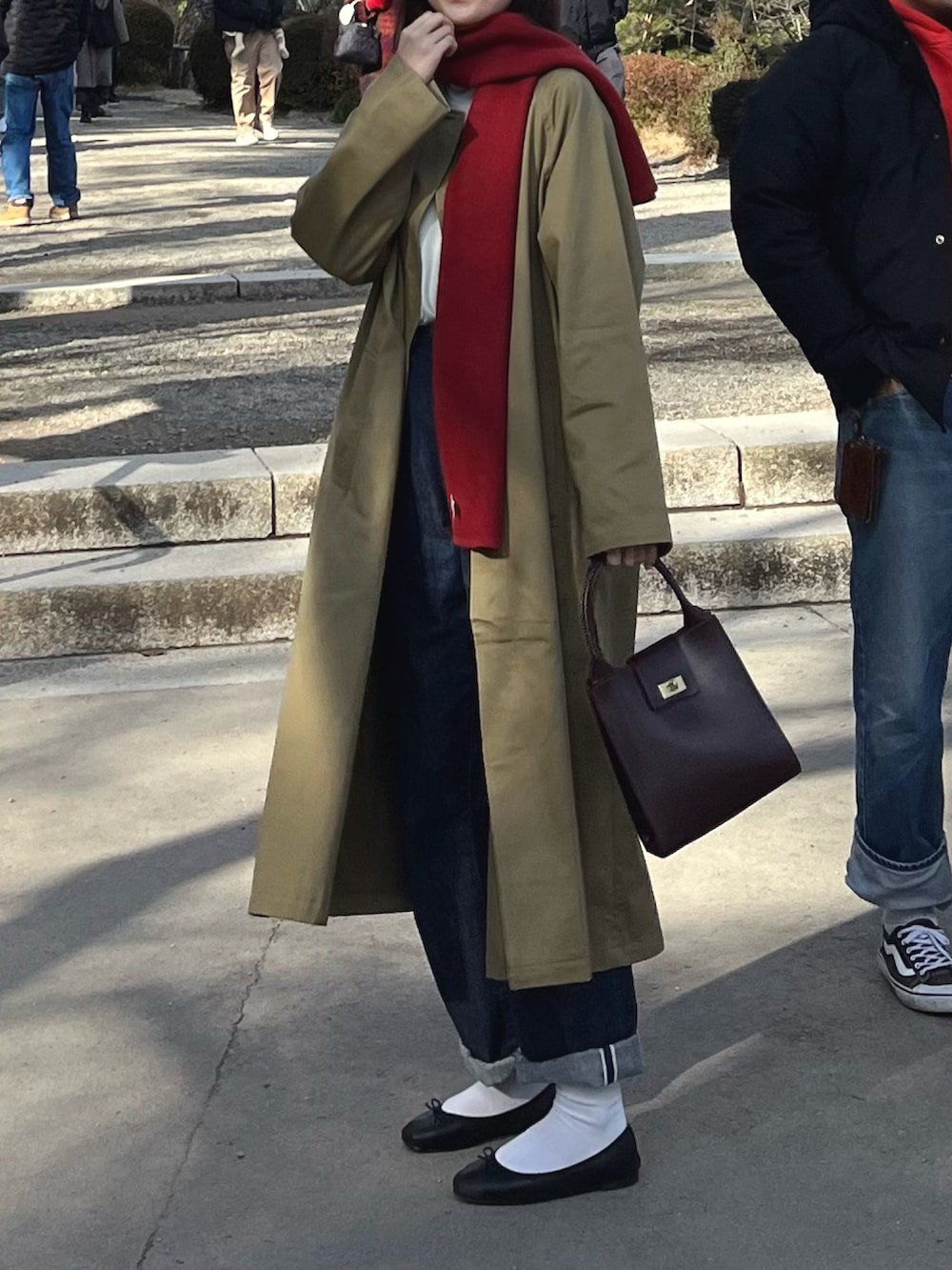 ベージュ系のステンカラーコート、レッド系のトートバッグ、ブラック系のバレエシューズを着用したレディースの冬コーディネートの2枚目の写真