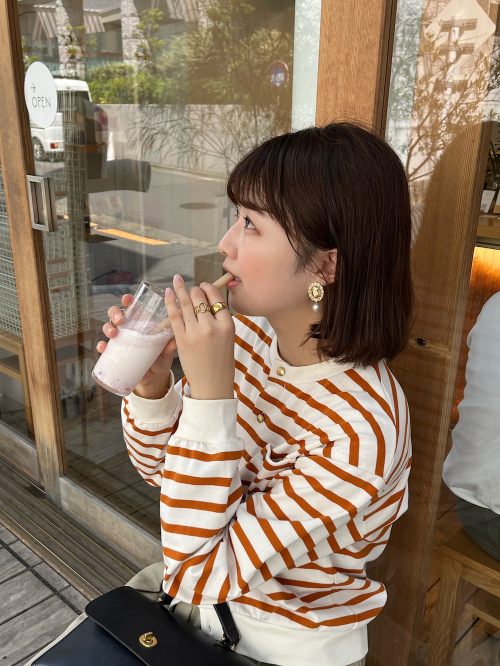 オレンジ系のカーディガン/ボレロ、ベージュ系のスカート、ブラック系のローファーを着用したレディースの夏コーディネートの2枚目の写真