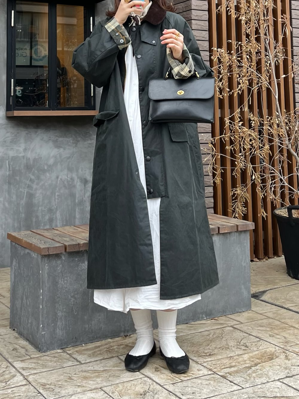 ホワイト系のシャツワンピース、ブラック系のショルダーバッグ、グリーン系のステンカラーコートを着用したレディースの冬コーディネートの2枚目の写真