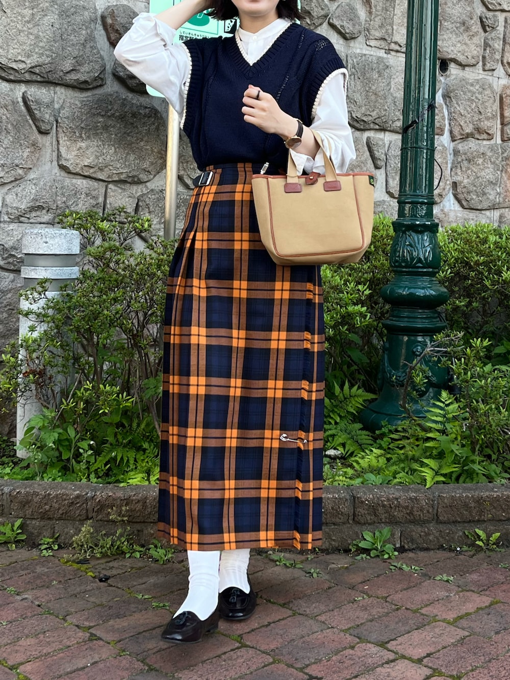 オレンジ系のスカート、グリーン系のトートバッグ、ブルー系のニット/セーターを着用したレディースの春コーディネートの2枚目の写真