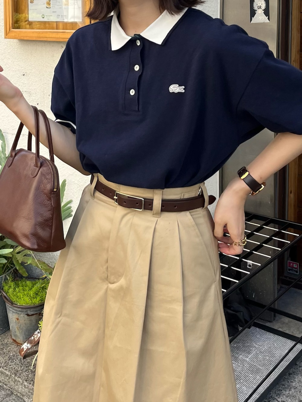 ブラウン系のモカシン/デッキシューズ、ブルー系のポロシャツ、ブラウン系のハンドバッグを着用したレディースの夏コーディネートの2枚目の写真