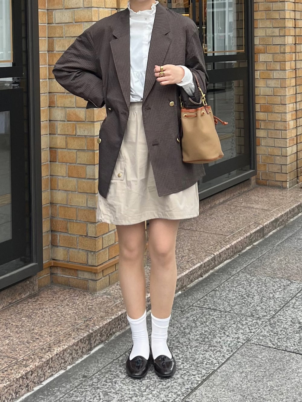 ブラウン系のローファー、ベージュ系のスカート、グリーン系のショルダーバッグを着用したレディースの春コーディネートの2枚目の写真