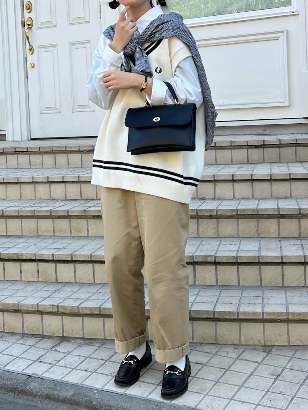 ホワイト系のベスト、ブラック系のショルダーバッグ、ベージュ系のチノパンツを着用したレディースの春コーディネートの2枚目の写真