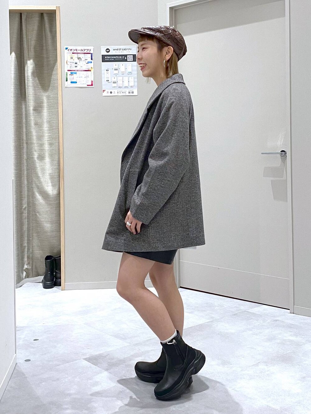 グレー系のチェスターコート、ブラウン系のニット/セーター、ブラック系のショルダーバッグを着用したレディースの秋コーディネートの2枚目の写真