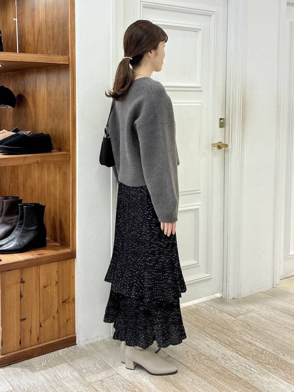 ベージュ系のブーツ、グレー系のスカート、ブラック系のショルダーバッグを着用したレディースの秋コーディネートの2枚目の写真