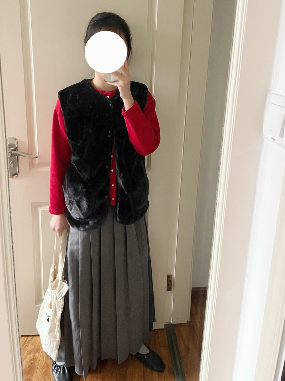 ブラック系のベスト、グレー系のスカート、ベージュ系のトートバッグを着用したレディースの冬コーディネートの2枚目の写真