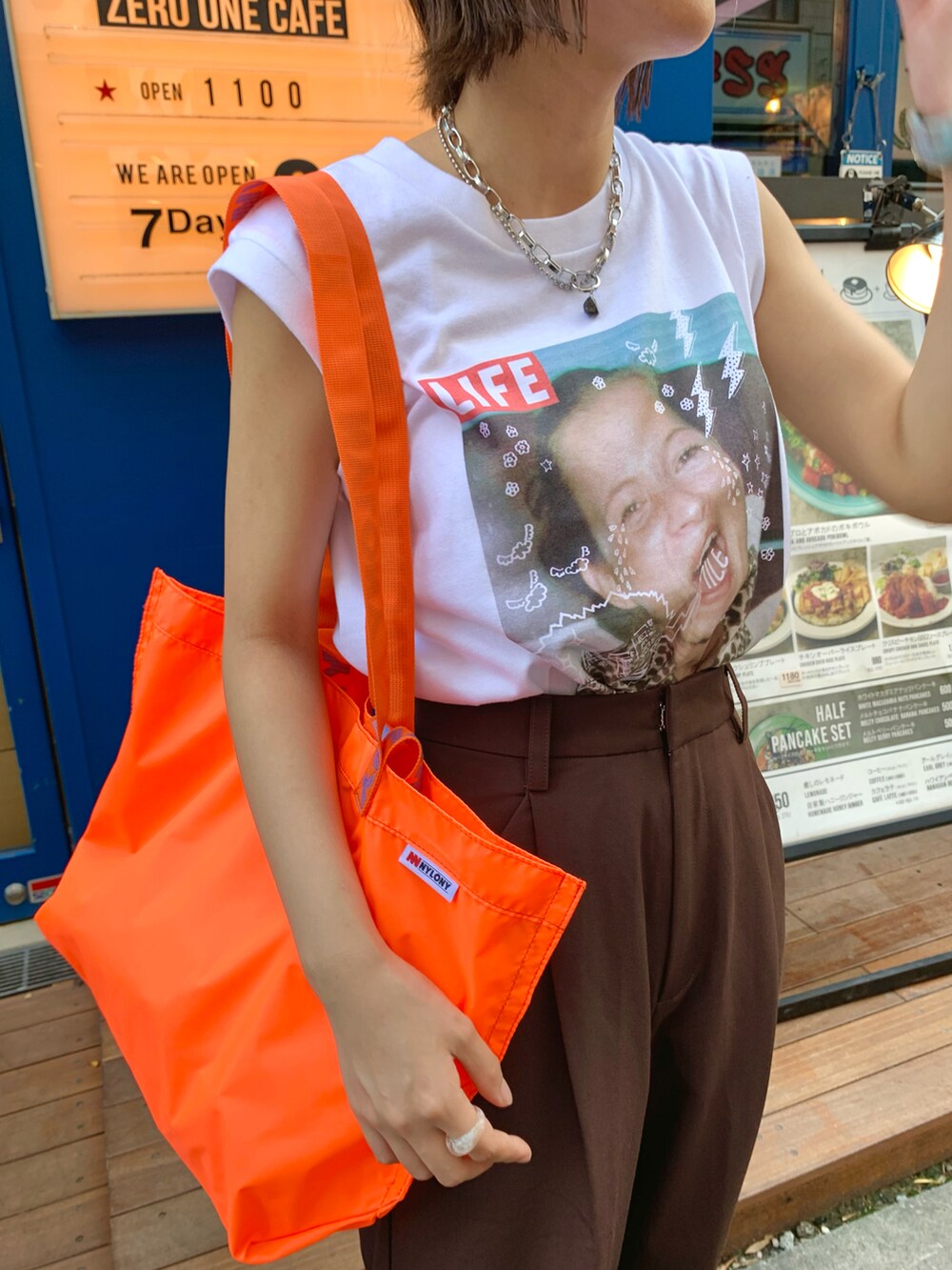オレンジ系のトートバッグ、ホワイト系のTシャツ/カットソー、ブラウン系のスラックスを着用したレディースの夏コーディネートの2枚目の写真