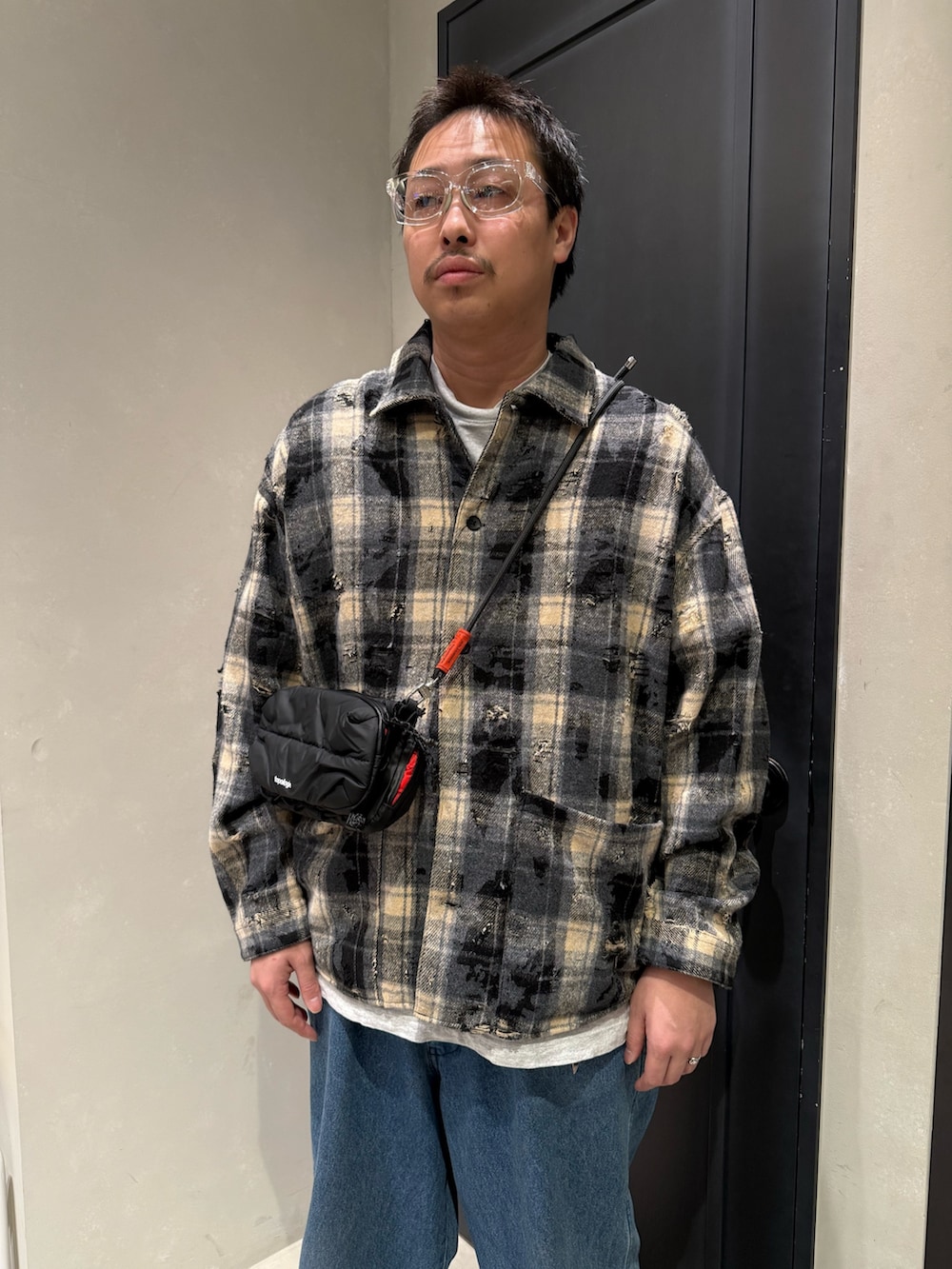 ブルー系のデニムパンツ、ブラック系のスニーカー、ブラック系のショルダーバッグを着用したメンズの秋コーディネートの3枚目の写真