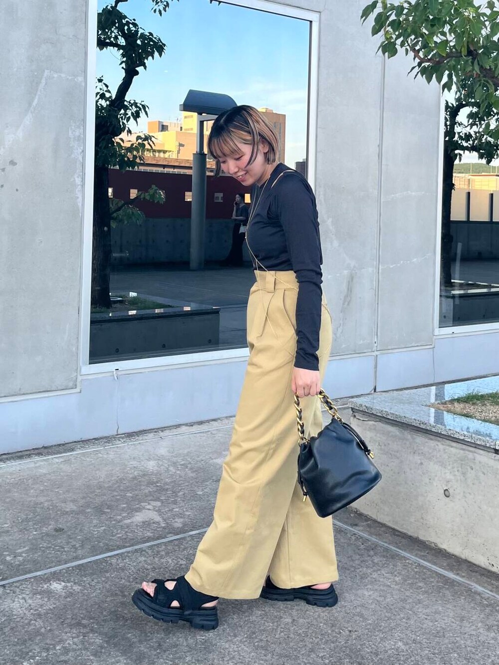 ブラック系のショルダーバッグ、ブラック系のサンダル、ベージュ系のチノパンツを着用したレディースの夏コーディネートの2枚目の写真