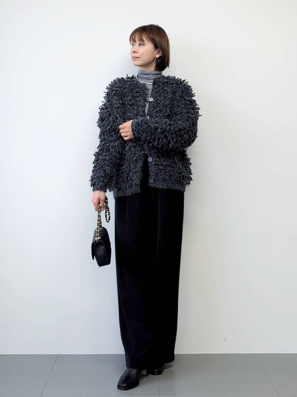 ブラック系のスラックス、ブラック系のブーツ、グレー系のカーディガン/ボレロを着用したレディースの秋コーディネートの5枚目の写真