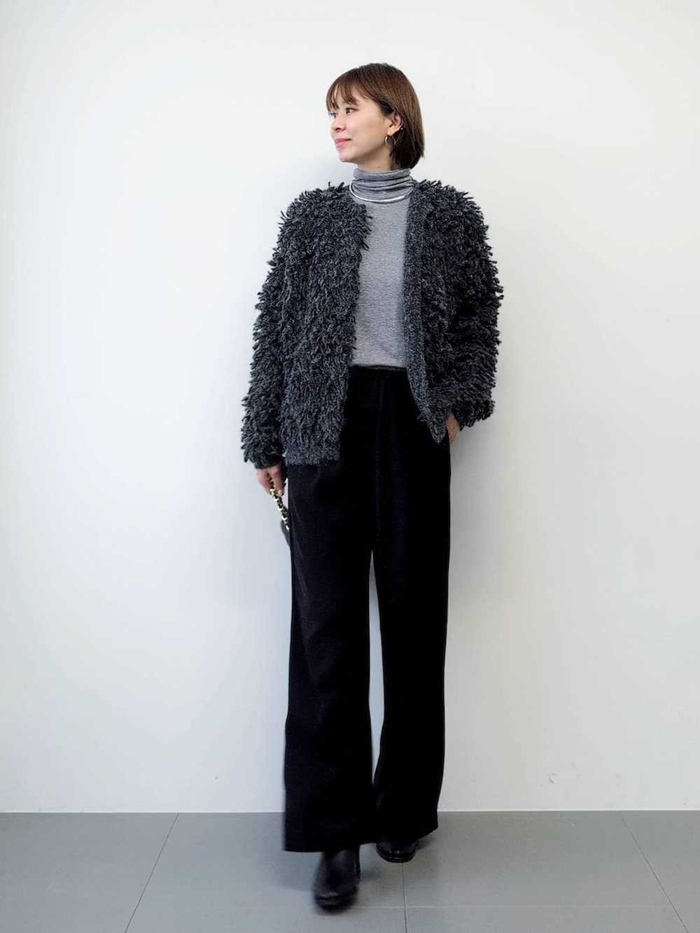 ブラック系のスラックス、ブラック系のブーツ、グレー系のカーディガン/ボレロを着用したレディースの秋コーディネートの2枚目の写真