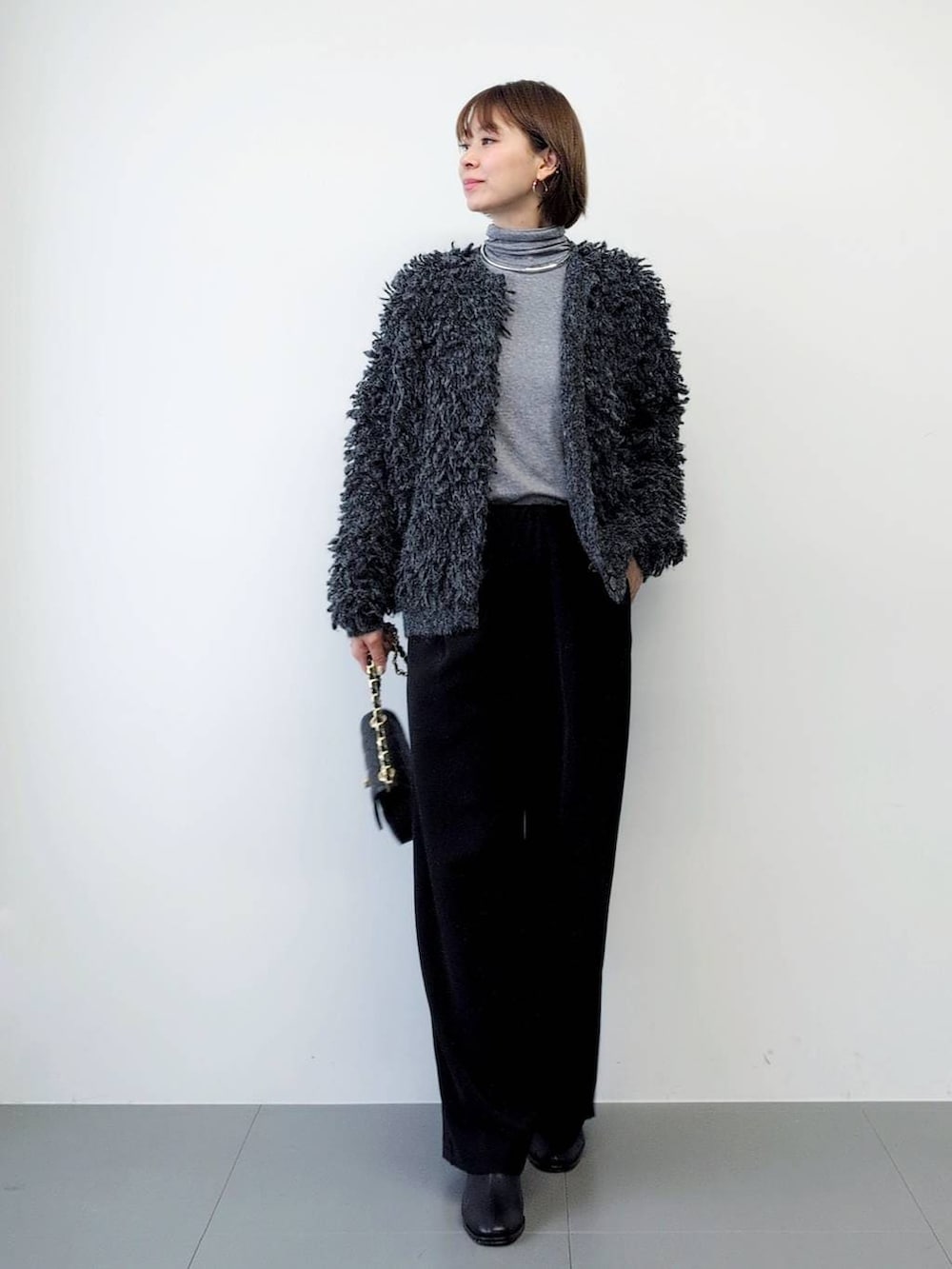 ブラック系のスラックス、ブラック系のブーツ、グレー系のカーディガン/ボレロを着用したレディースの秋コーディネートの3枚目の写真