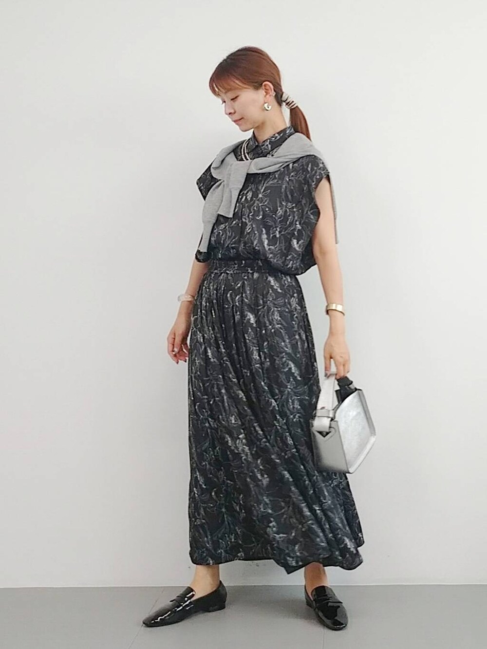 シルバー系のハンドバッグ、ブラック系のレインシューズ、グレー系のカーディガン/ボレロを着用したレディースの夏コーディネートの2枚目の写真