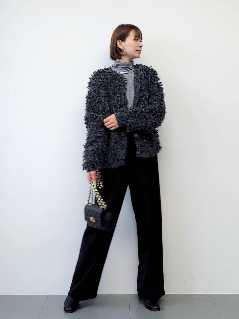 ブラック系のスラックス、ブラック系のブーツ、グレー系のカーディガン/ボレロを着用したレディースの秋コーディネートの4枚目の写真