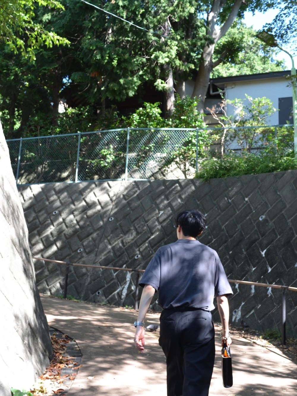 グレー系のポロシャツ、ブラック系のハンドバッグ、ブラック系のスラックスを着用したメンズの秋コーディネートの3枚目の写真