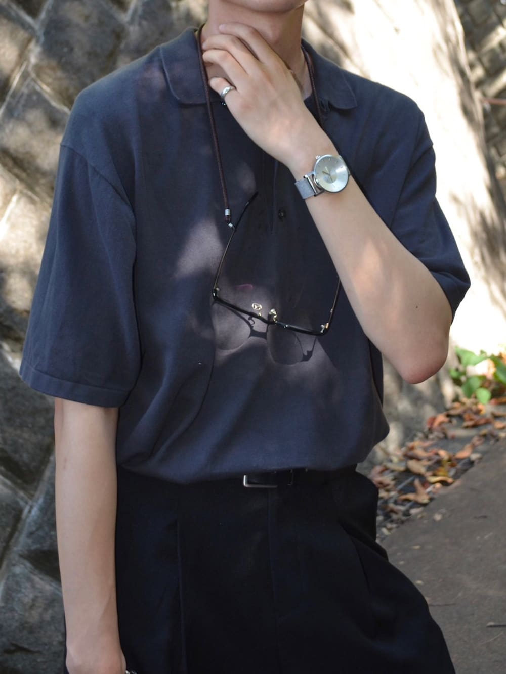 グレー系のポロシャツ、ブラック系のハンドバッグ、ブラック系のスラックスを着用したメンズの秋コーディネートの2枚目の写真