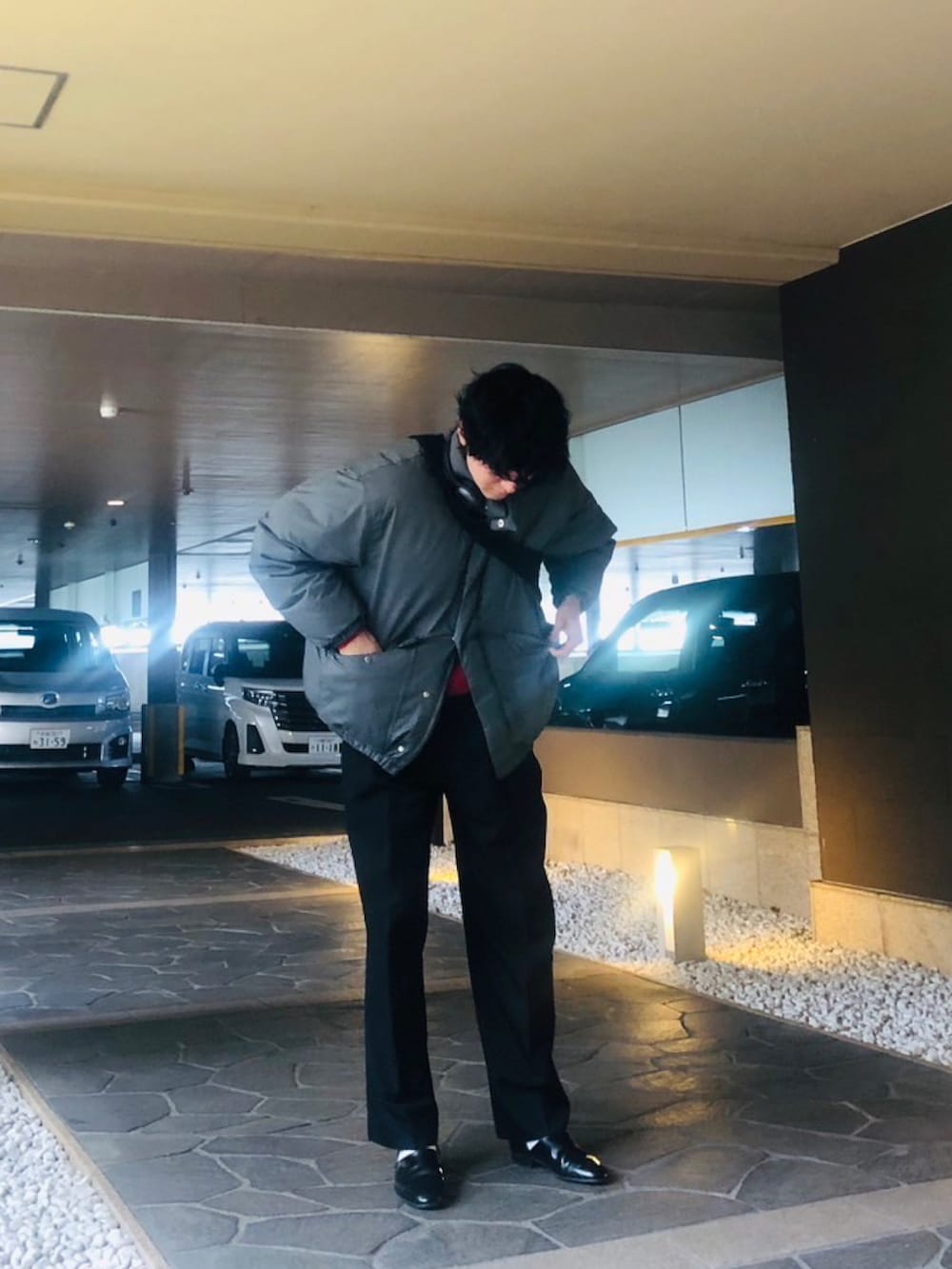 ブラック系のスラックス、ブラック系のスリッポン、グレー系のダウンジャケット/コートを着用したメンズの春コーディネートの2枚目の写真