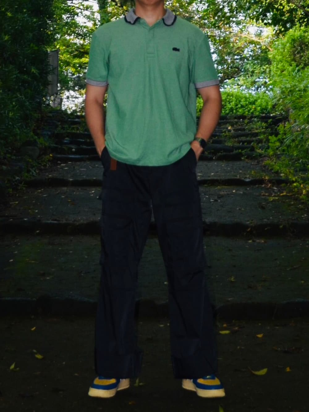 グリーン系のポロシャツ、ブラック系のカーゴパンツ、ブルー系のスニーカーを着用したメンズの秋コーディネートの2枚目の写真
