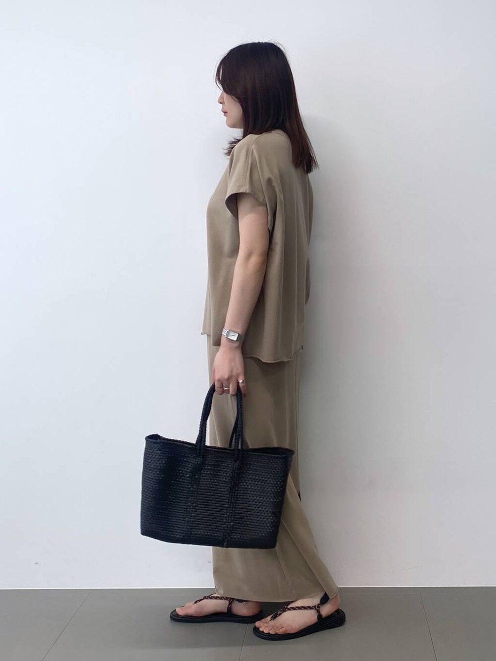 ブラック系のトートバッグ、ブラウン系のサンダル、ベージュ系のTシャツ/カットソーを着用したレディースの春コーディネートの2枚目の写真