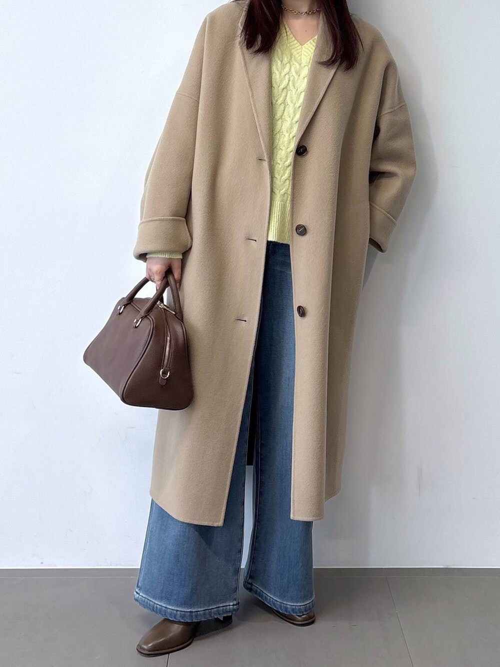 ブラウン系のボストンバッグ、ブルー系のデニムパンツ、ベージュ系のチェスターコートを着用したレディースの秋コーディネートの2枚目の写真