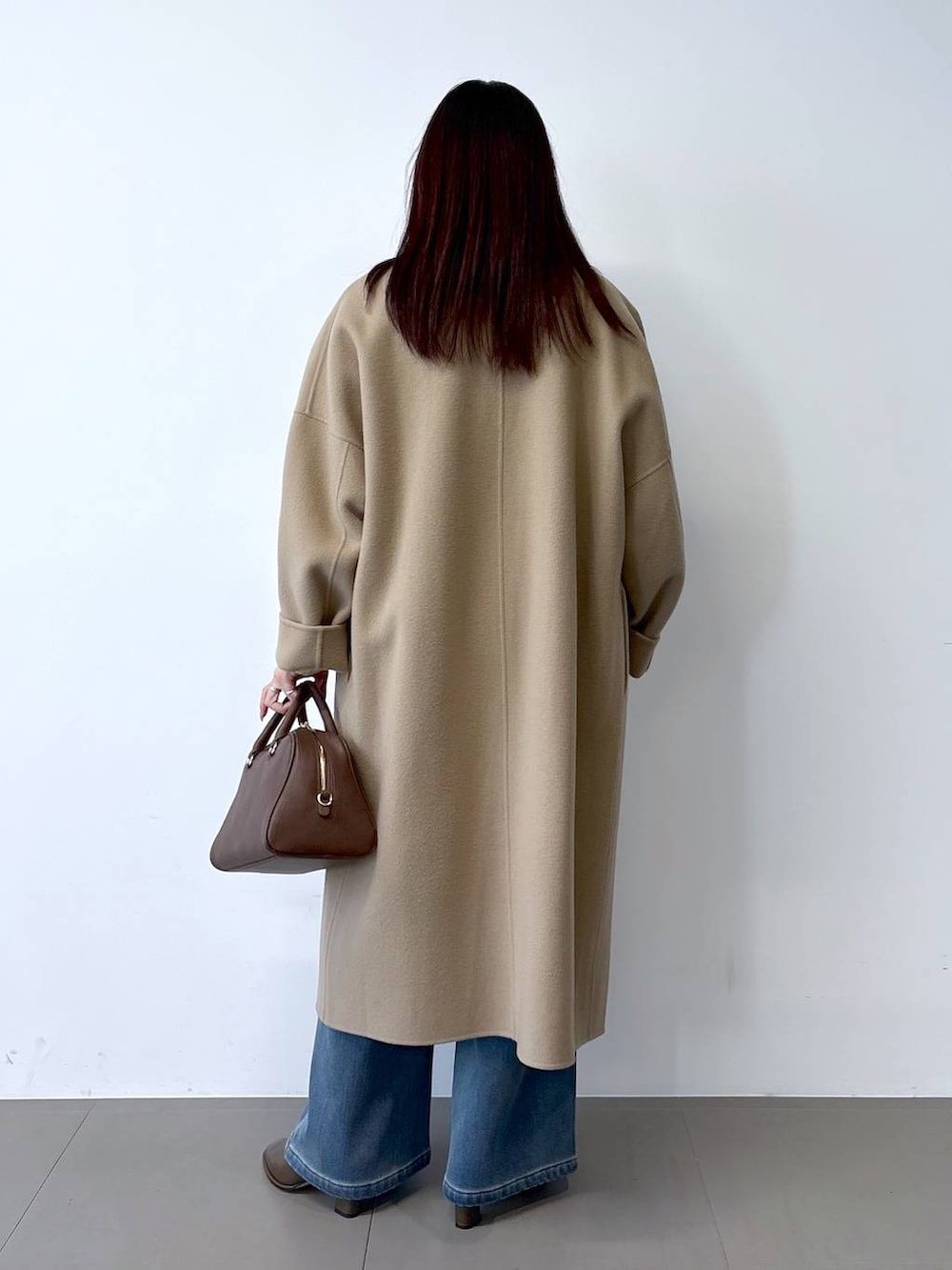 ブラウン系のボストンバッグ、ブルー系のデニムパンツ、ベージュ系のチェスターコートを着用したレディースの秋コーディネートの4枚目の写真