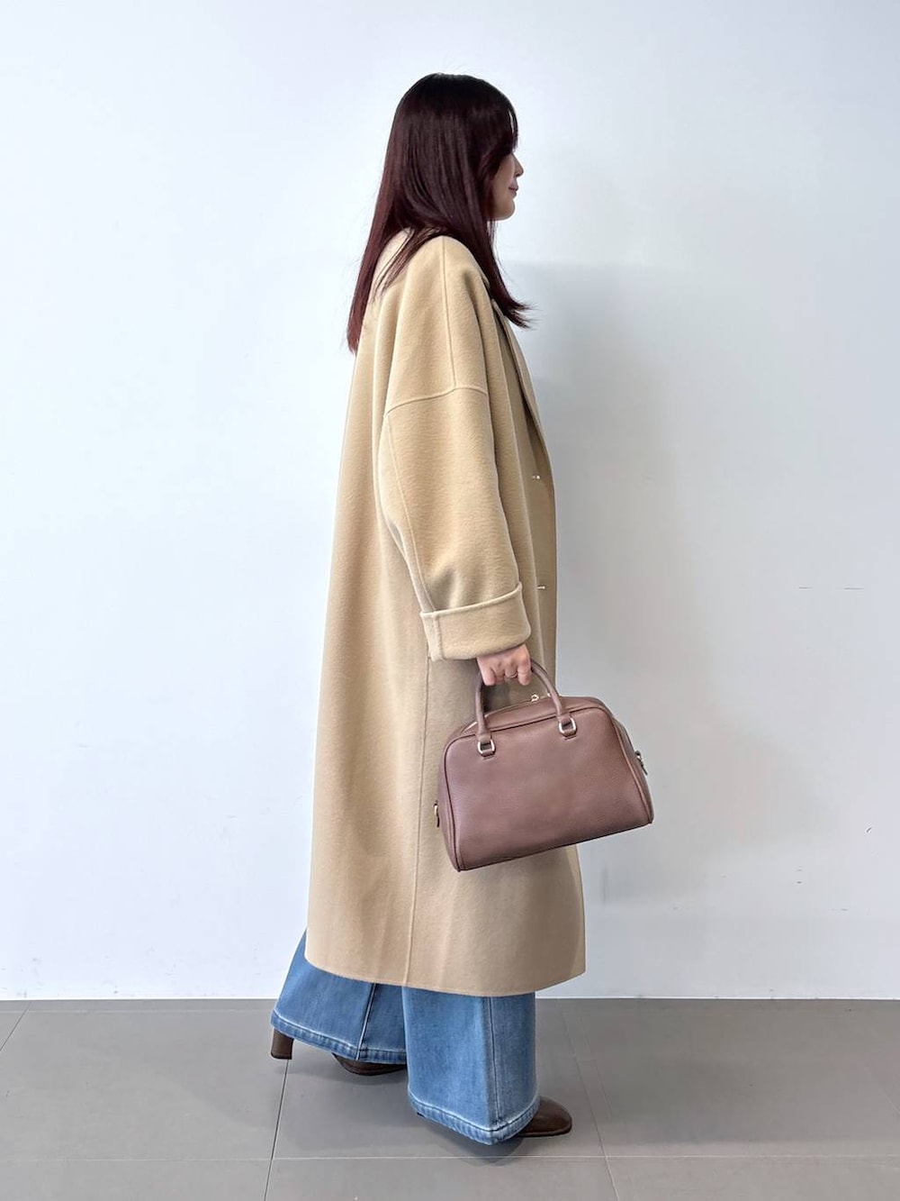 ブラウン系のボストンバッグ、ブルー系のデニムパンツ、ベージュ系のチェスターコートを着用したレディースの秋コーディネートの3枚目の写真