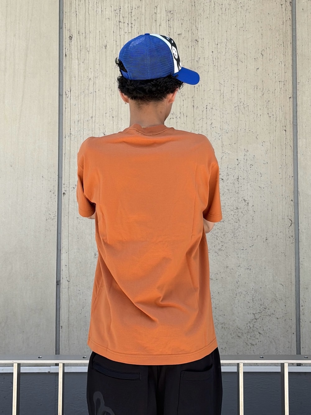 オレンジ系のTシャツ/カットソー、ブラック系のスウェットパンツ、ブルー系のキャップを着用したメンズの春コーディネートの8枚目の写真