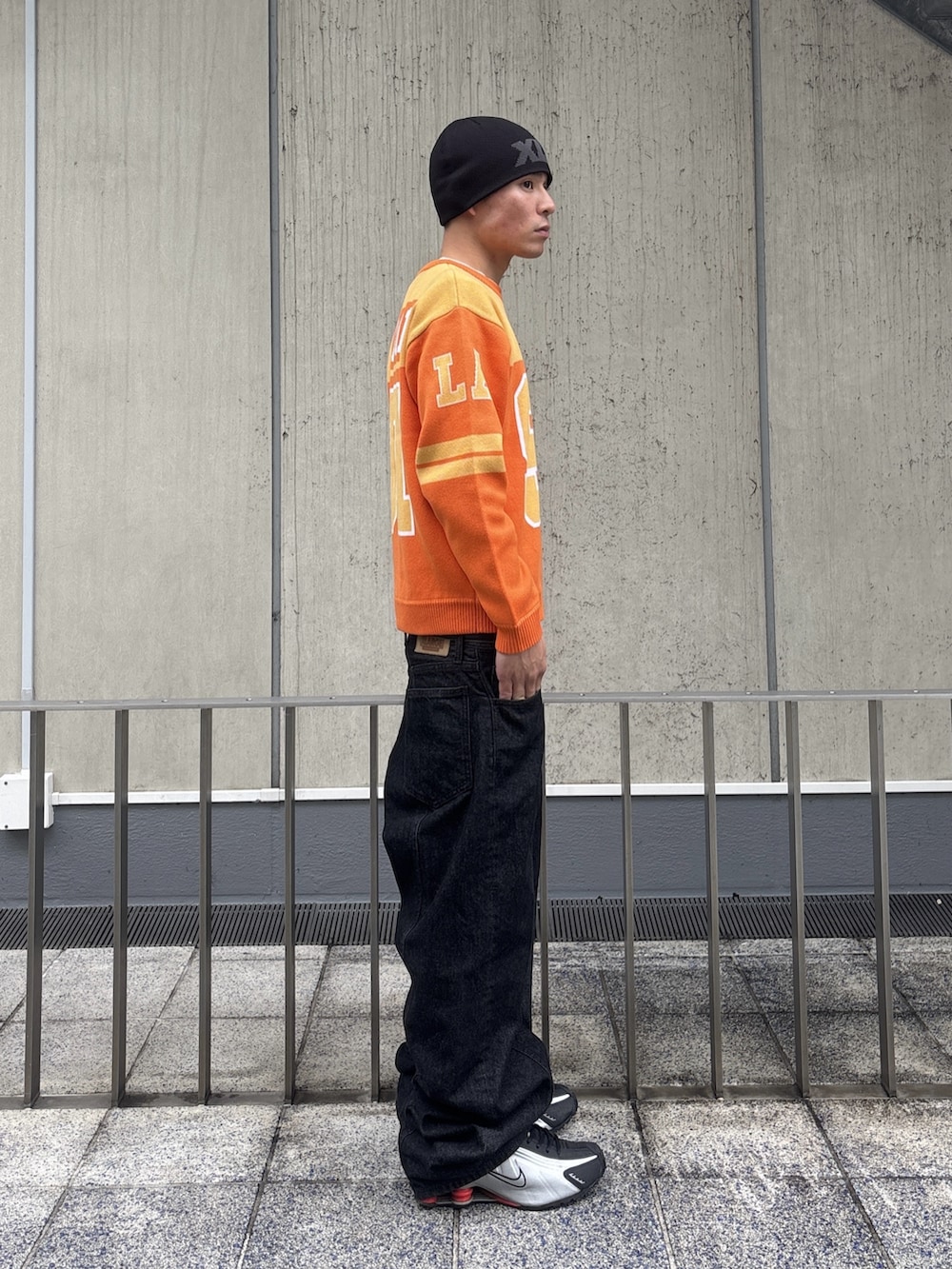 オレンジ系のニット/セーター、ブラック系のデニムパンツ、ピンク系のニットキャップ/ビーニーを着用したメンズの冬コーディネートの3枚目の写真