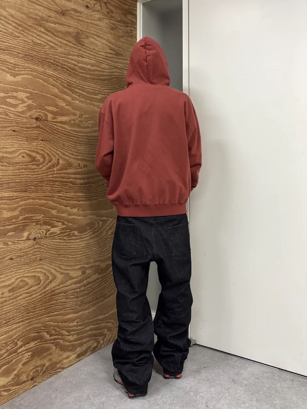 レッド系のパーカー、ブラック系のデニムパンツを着用したメンズの冬コーディネートの5枚目の写真