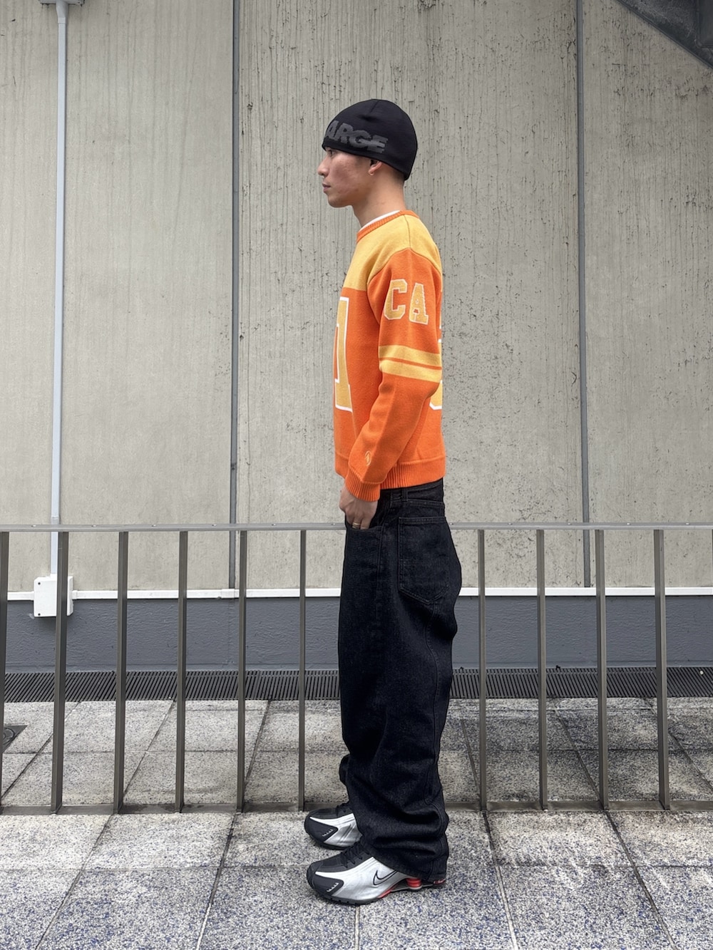 オレンジ系のニット/セーター、ブラック系のデニムパンツ、ピンク系のニットキャップ/ビーニーを着用したメンズの冬コーディネートの2枚目の写真