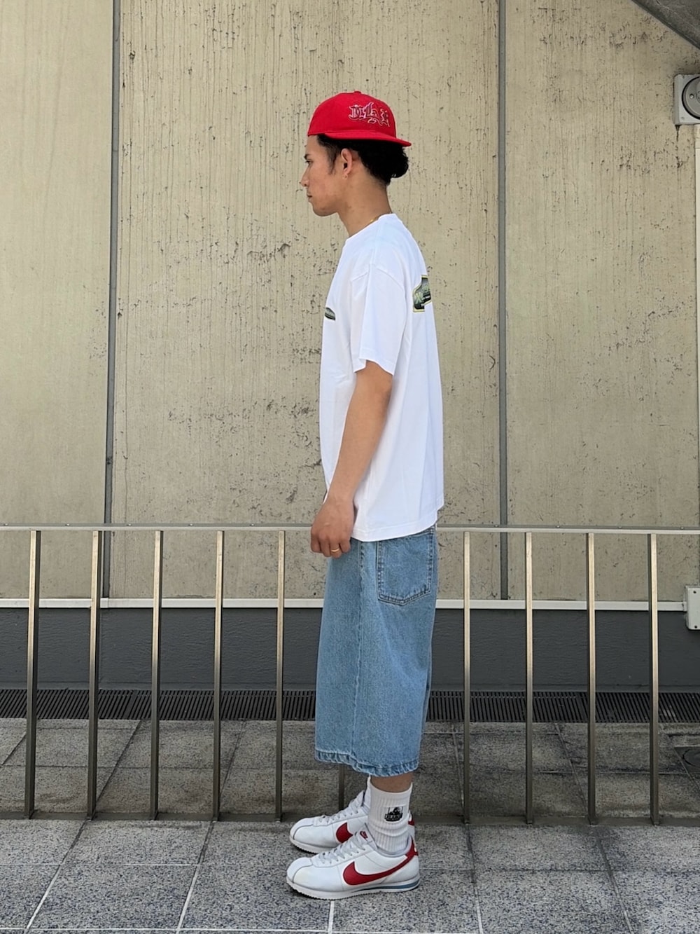 グリーン系のデニムパンツ、ホワイト系のTシャツ/カットソー、レッド系のキャップを着用したメンズの春コーディネートの2枚目の写真