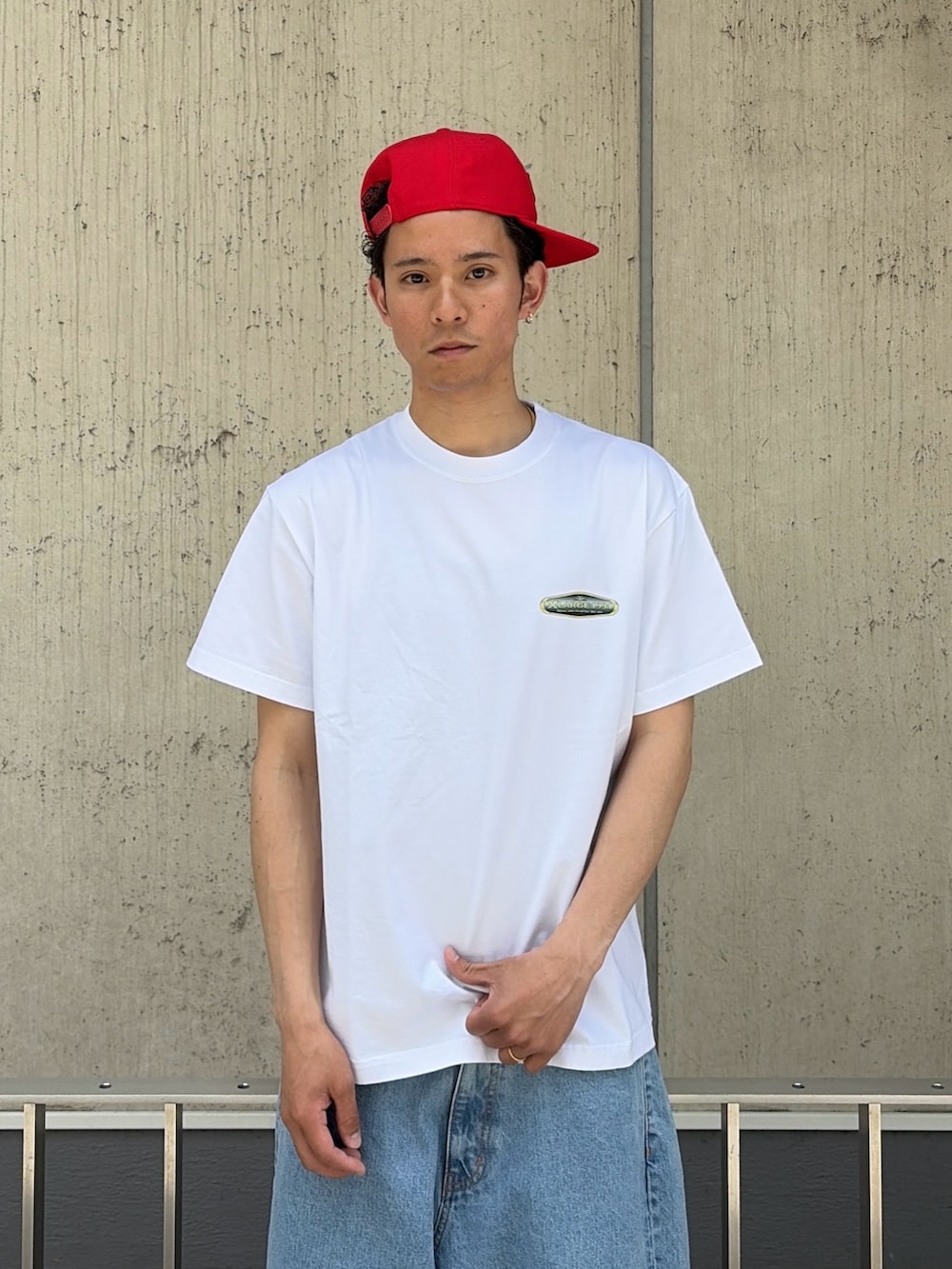 グリーン系のデニムパンツ、ホワイト系のTシャツ/カットソー、レッド系のキャップを着用したメンズの春コーディネートの5枚目の写真